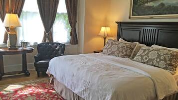 A neatly made bed with a floral-patterned pillow, a red patterned rug, and a painting above the bed.