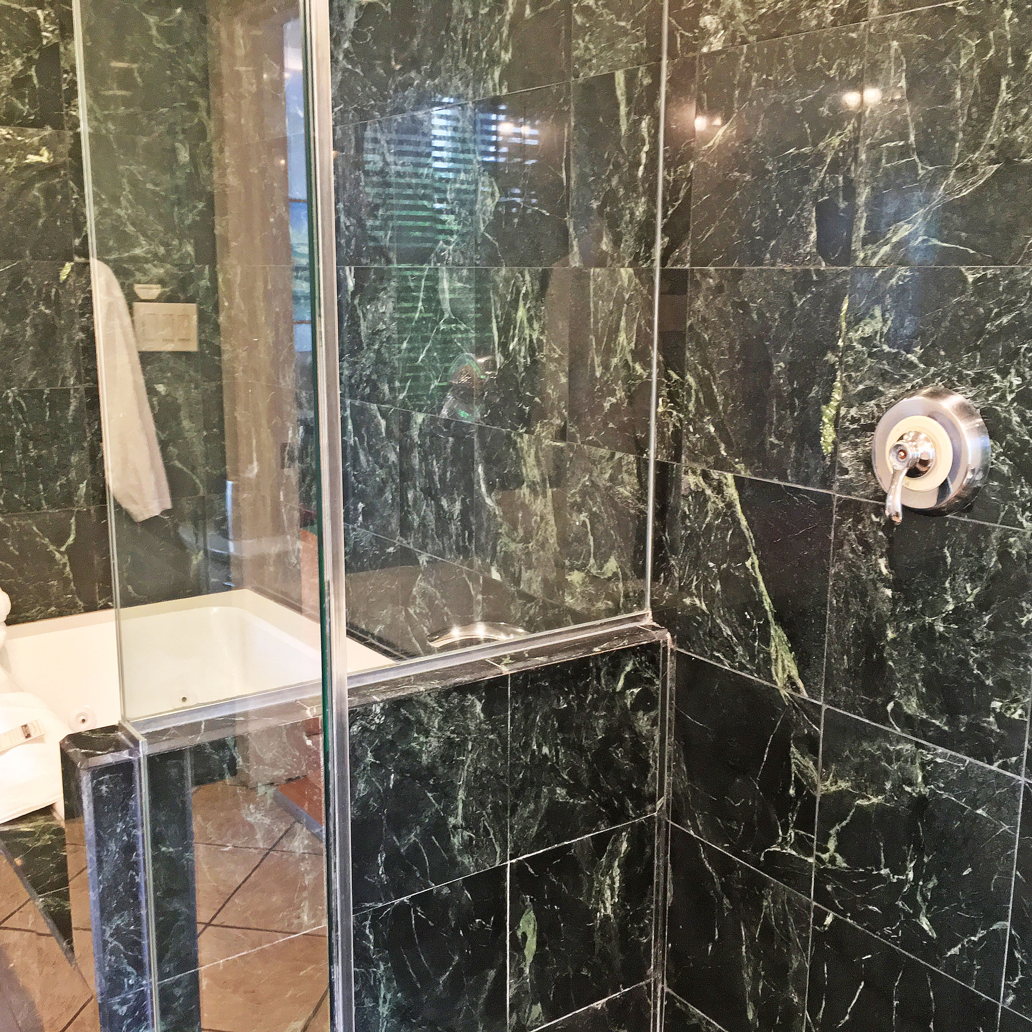 Une salle de bain dotée d’une douche à parois de verre, d’une baignoire blanche et d’un mur recouvert de carreaux de marbre.