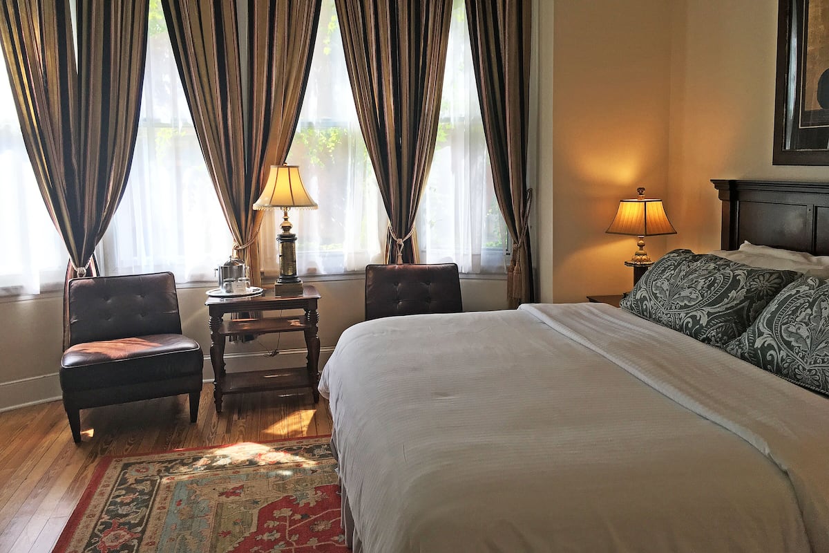 A hotel room with a large bed, two bedside tables with lamps, a chair, and a window with curtains.