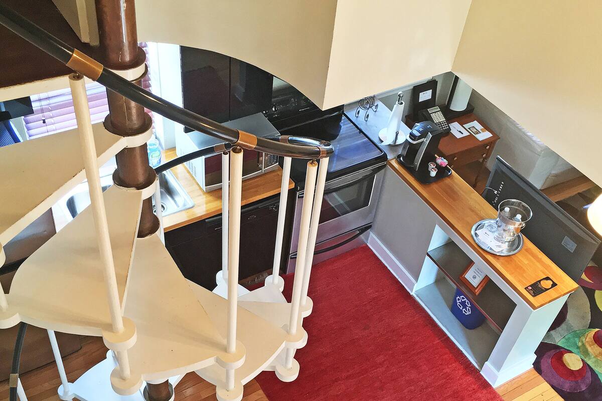 A staircase with a white railing, a red rug on the floor, and a kitchen area with a microwave, oven, and coffee maker.