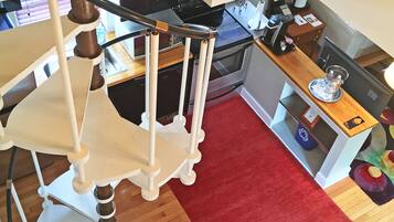 A staircase with a white railing, a red rug on the floor, and a kitchen area with a microwave, oven, and coffee maker.
