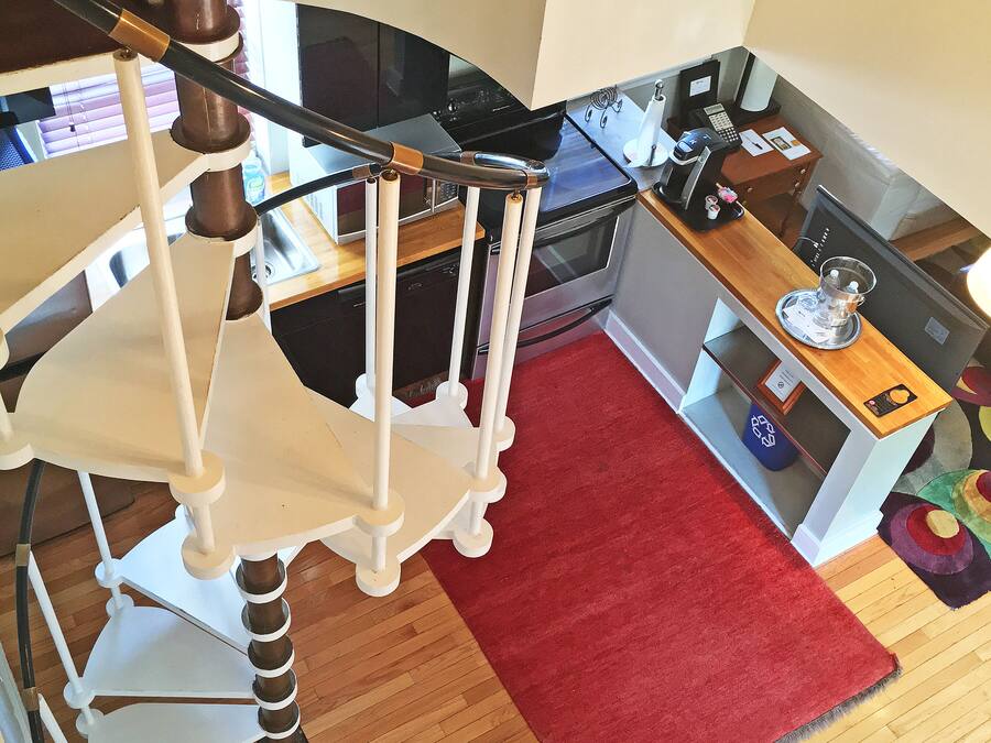 A staircase with a white railing, a red rug on the floor, and a kitchen area with a microwave, oven, and coffee maker.