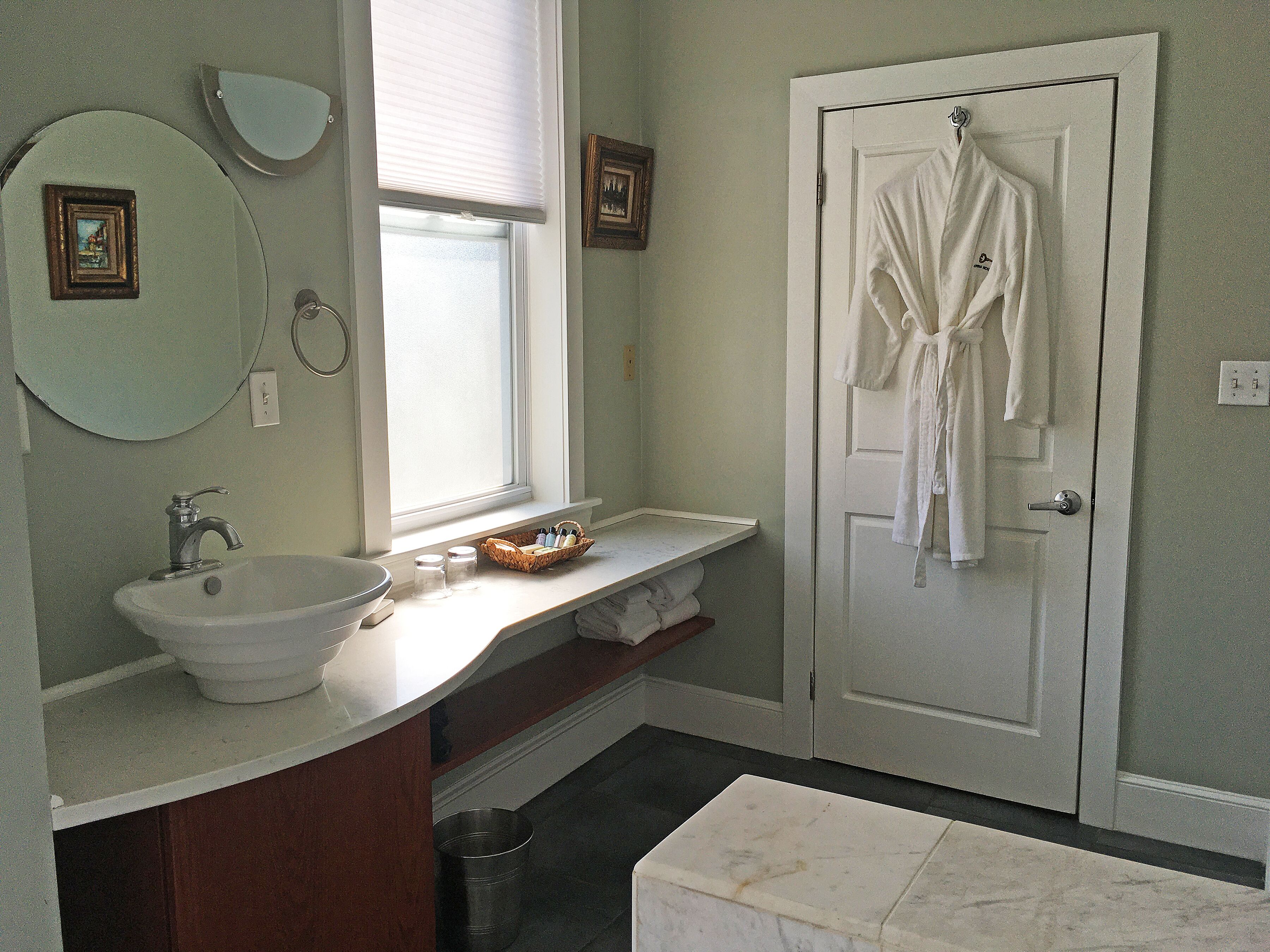 A bathroom with a sink, mirror, and a door with a robe hanging.