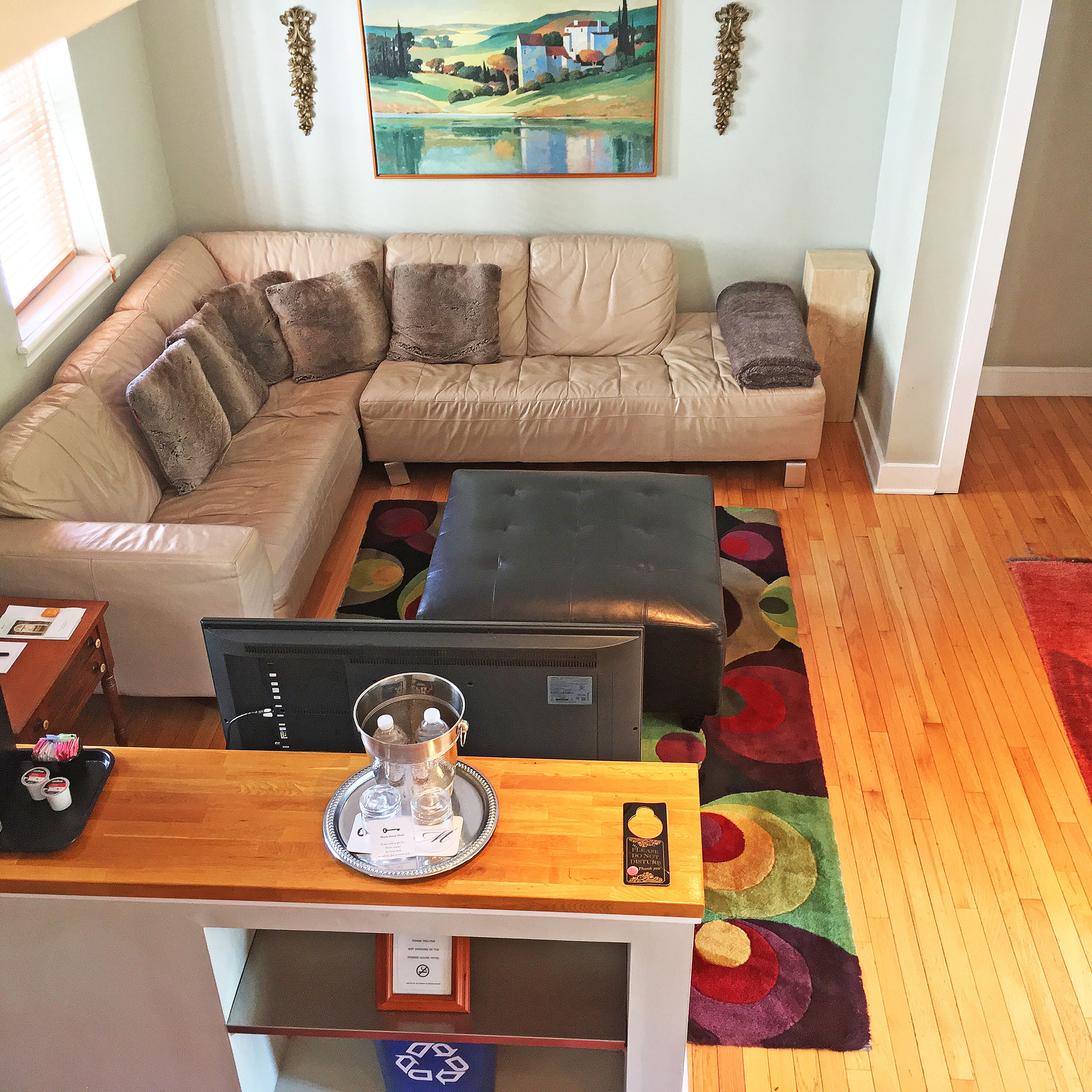 A living room with a sectional sofa, a coffee table, and a desk with a computer. There is a painting on the wall and a rug on the floor.