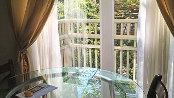 A round glass table with a chair, curtains, and a view of a white fence and trees.