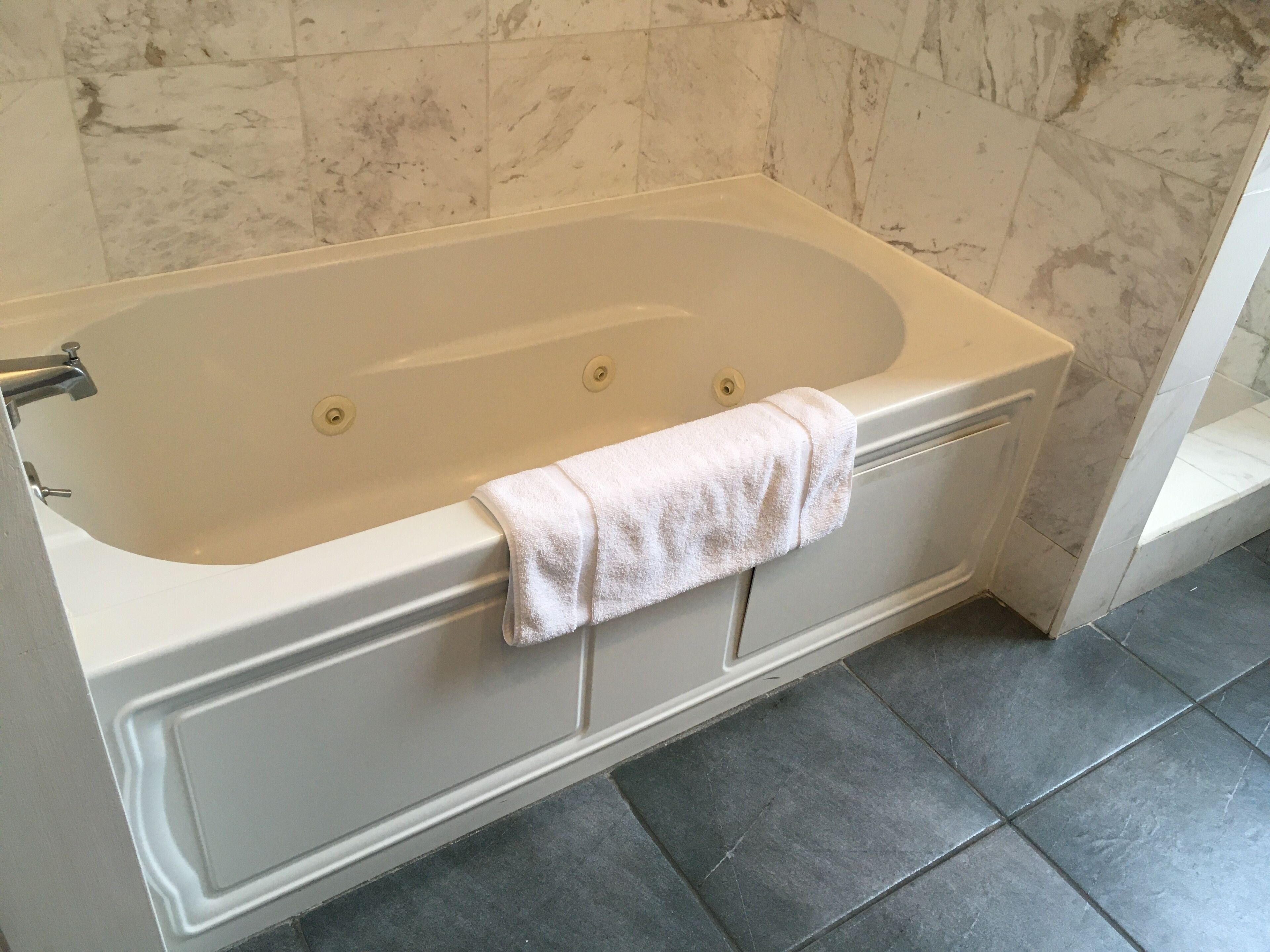 A modern bathroom with a freestanding bathtub, a towel hanging on the side, and marble tiles on the walls and floor.