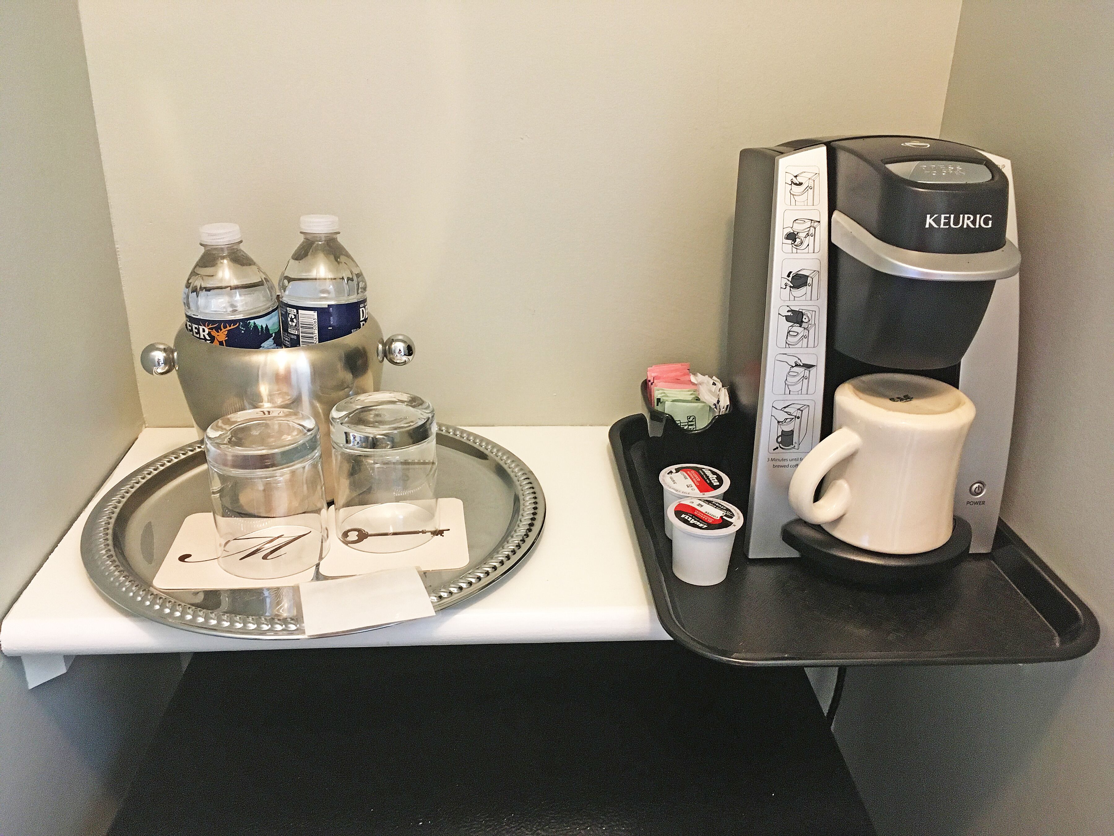 A coffee machine, two bottles of water, a mug, and a tray with a key and napkins.