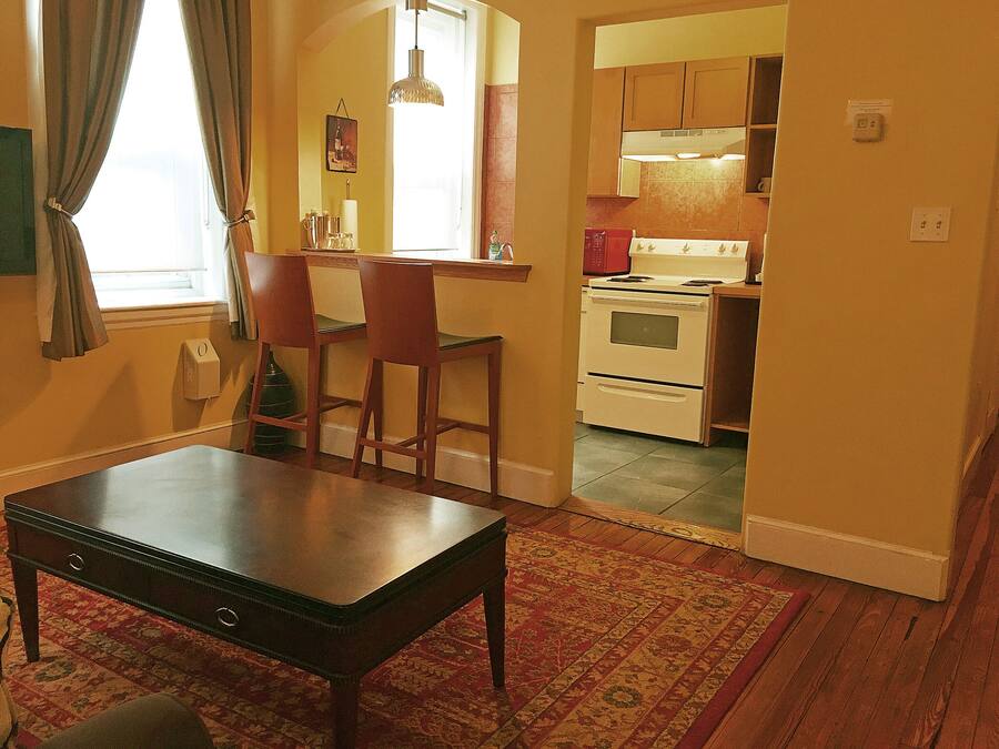 A dining area with a table and chairs, a kitchen visible through an open doorway, and a patterned rug on the floor.