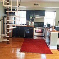 Una cocina con alfombra roja, electrodomésticos de acero inoxidable y una escalera blanca.