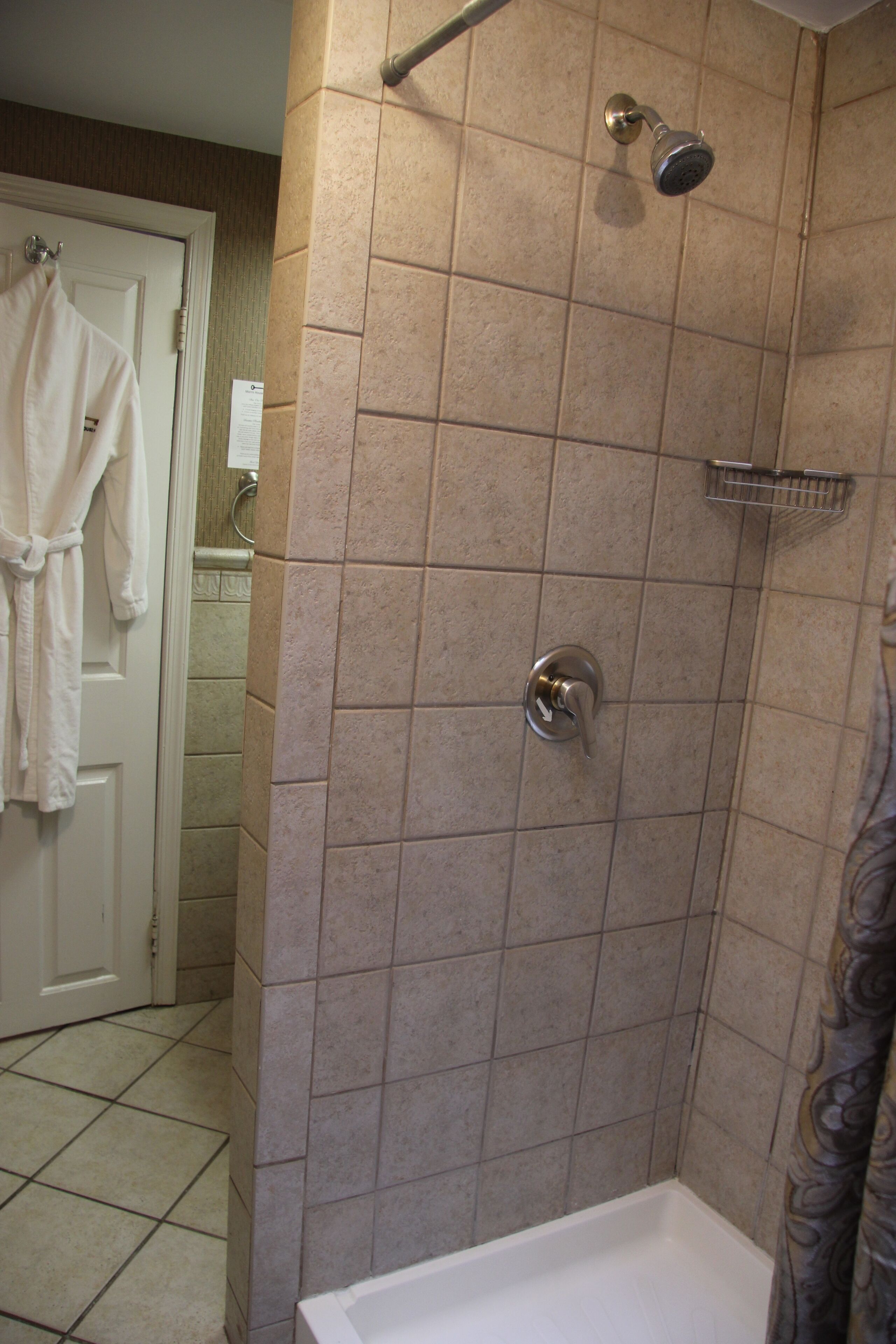 Un baño con ducha, paredes de azulejos, una bañera blanca y una puerta con una toalla colgada.