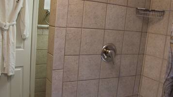 Un baño con ducha, paredes de azulejos, una bañera blanca y una puerta con una toalla colgada.