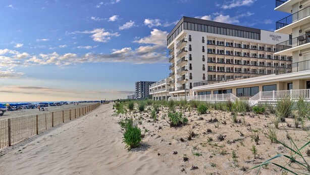 Un hotel frente a la playa con varios balcones y una playa de arena en primer plano.