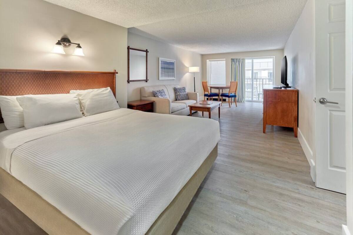 Habitación de hotel con una cama grande, un escritorio, una silla, un televisor y un balcón con vistas.