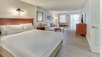 A hotel room with a large bed, a desk, a chair, a television, and a balcony with a view.