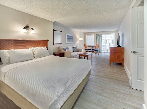 A hotel room with a large bed, a desk, a chair, a television, and a balcony with a view. - Henlopen Oceanfront Hotel (Rehoboth Beach)