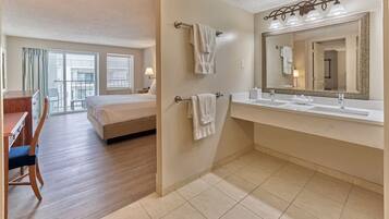 Habitación de hotel con cama, escritorio, silla y baño con lavamanos, espejo y toalleros.