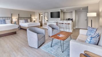 A hotel room with two beds, a sofa, a coffee table, a TV, a kitchen area, and a bathroom.