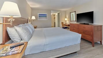 Quarto de hotel com uma cama grande, televisão, escrivaninha com abajur, cômoda e um quadro na parede.