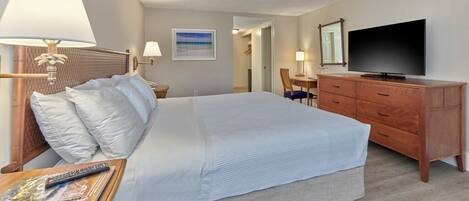 A hotel room with a large bed, a TV, a desk with a lamp, a dresser, and a painting on the wall.