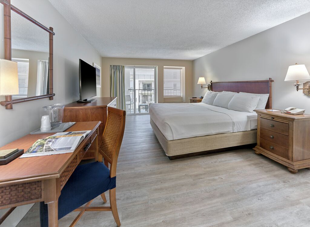 A hotel room with a bed, desk, chair, TV, and a view of the outside.