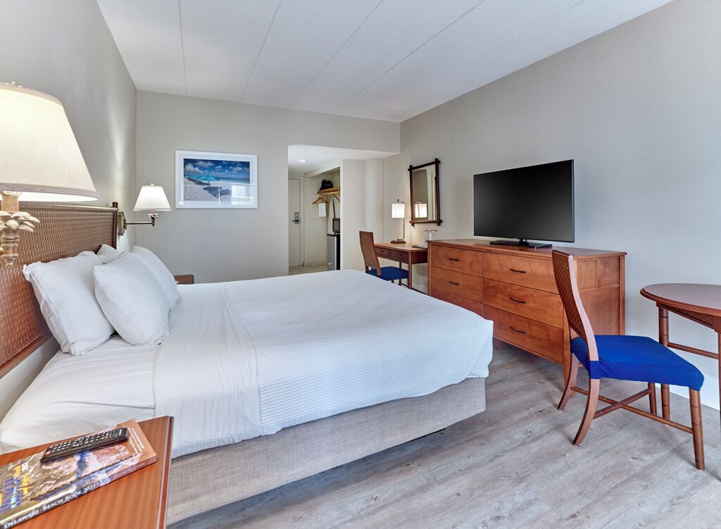 Ein Hotelzimmer mit einem großen Bett, einem Schreibtisch mit Fernseher, einem Sessel und einer Lampe.