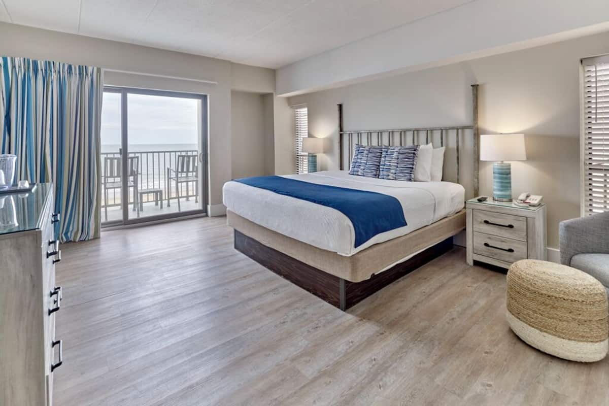 Habitación de hotel moderna con una cama grande, un balcón, un escritorio y una silla.
