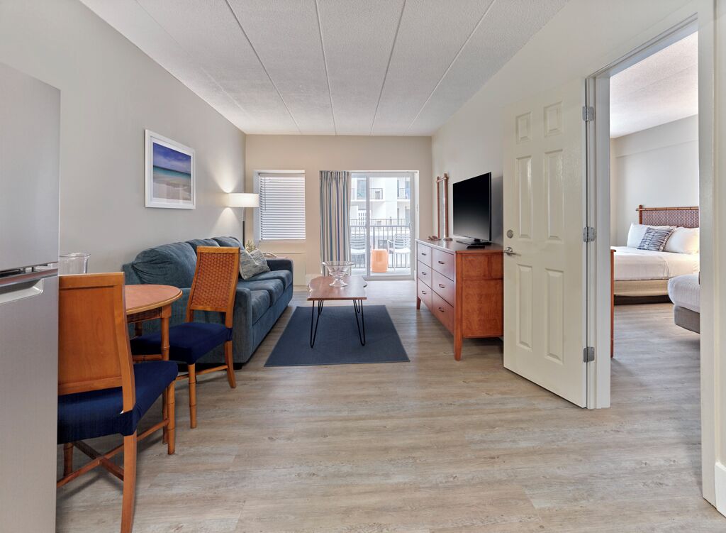 A compact hotel room with a sofa, a dining table with chairs, a TV, and a bed.