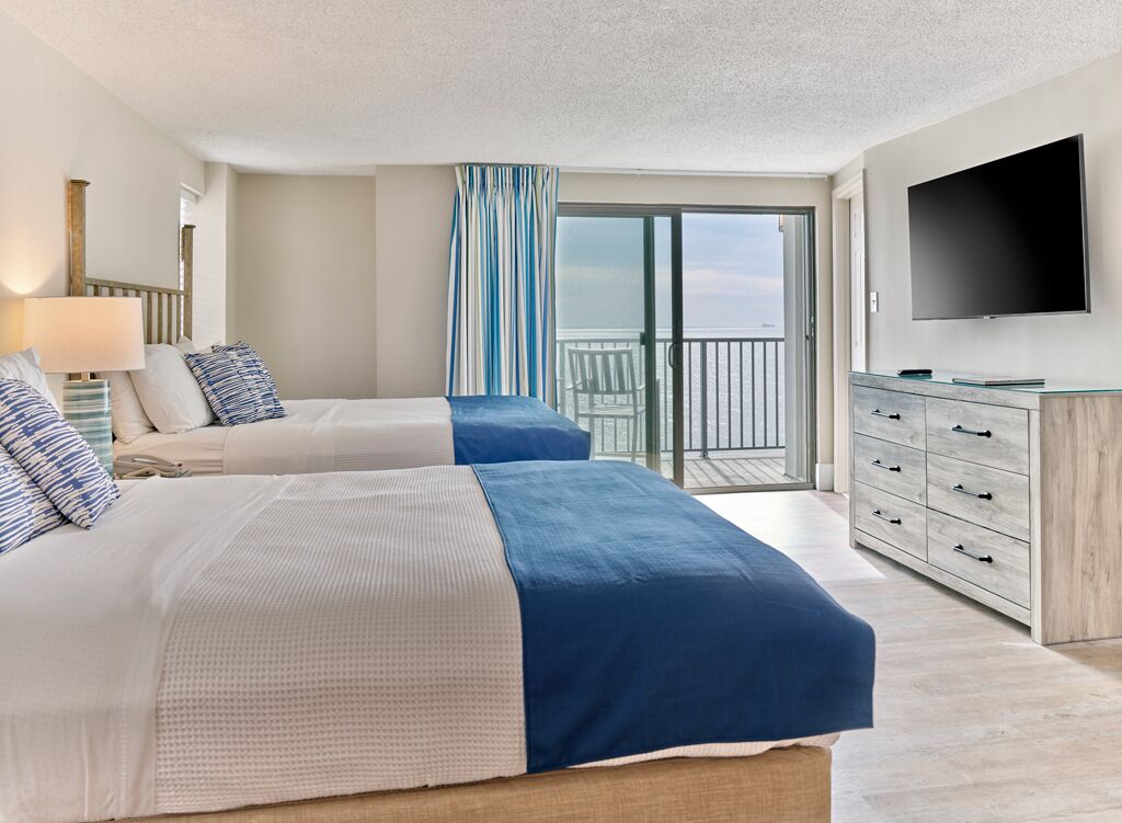 A hotel room with two beds, a TV, a balcony with a view, and a dresser.