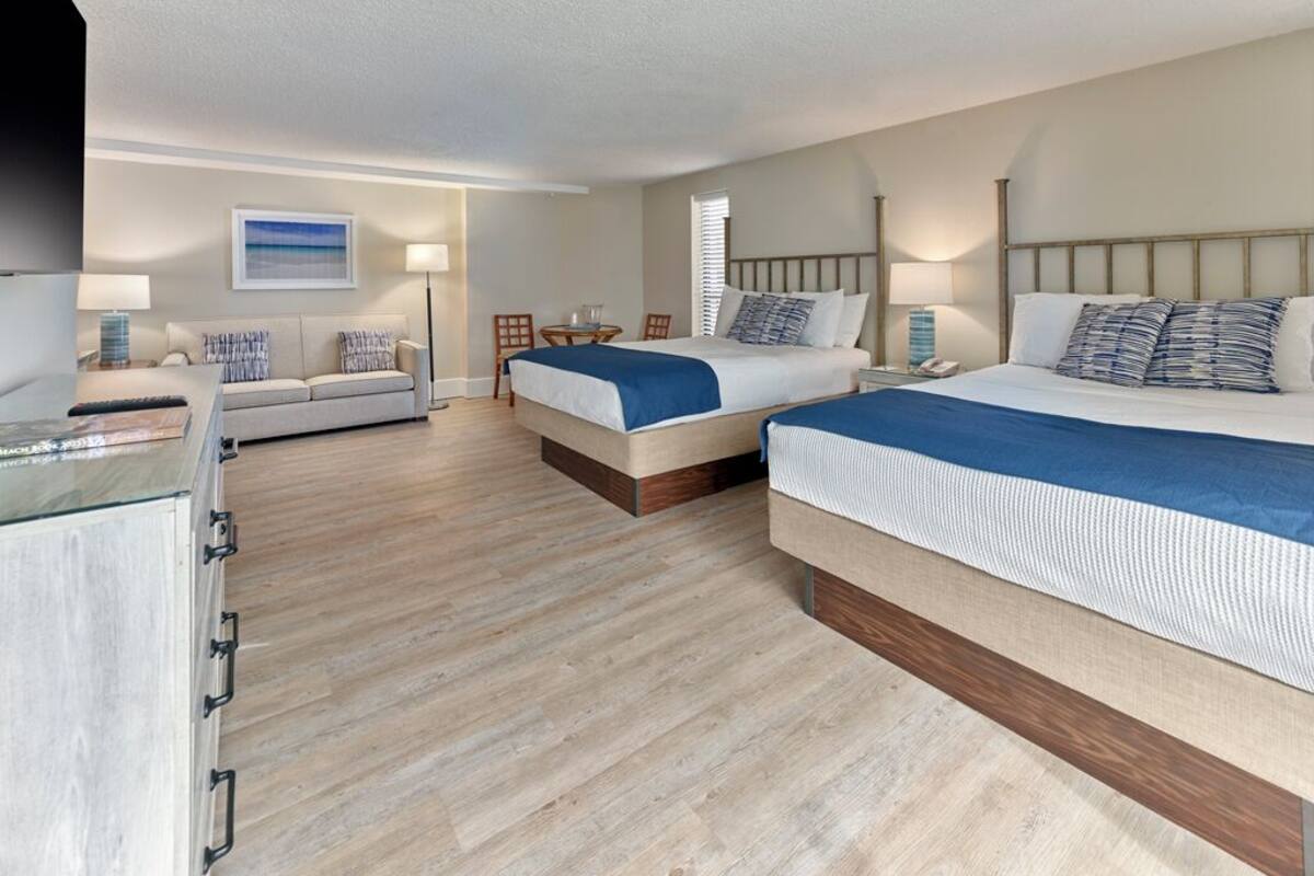 Habitación de hotel con dos camas, un sofá, un escritorio y una lámpara.