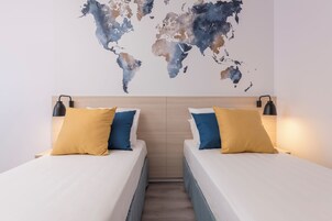 A hotel room with two beds, each with a yellow and blue pillow, and a world map on the wall.