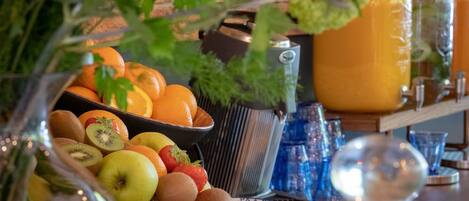 A table with a fruit bowl containing kiwis, apples, oranges, and strawberries, a large orange jug, and a metal container.