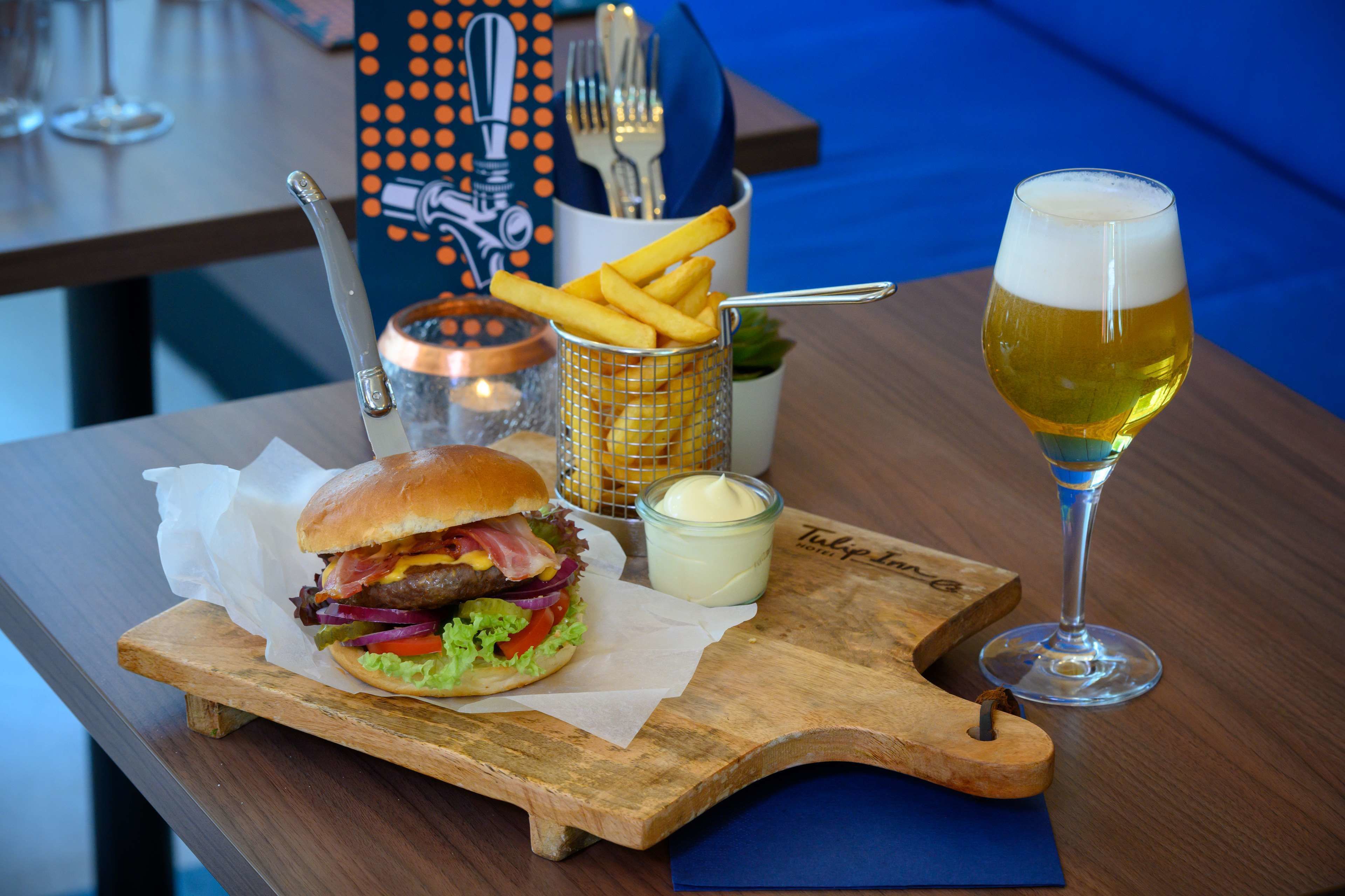 Un plato con una hamburguesa, papas fritas y una cerveza sobre una tabla de madera.