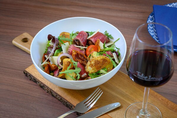 A bowl of salad with various ingredients and a glass of red wine on a wooden table. - Tulip Inn Antwerpen (Antwerp)
