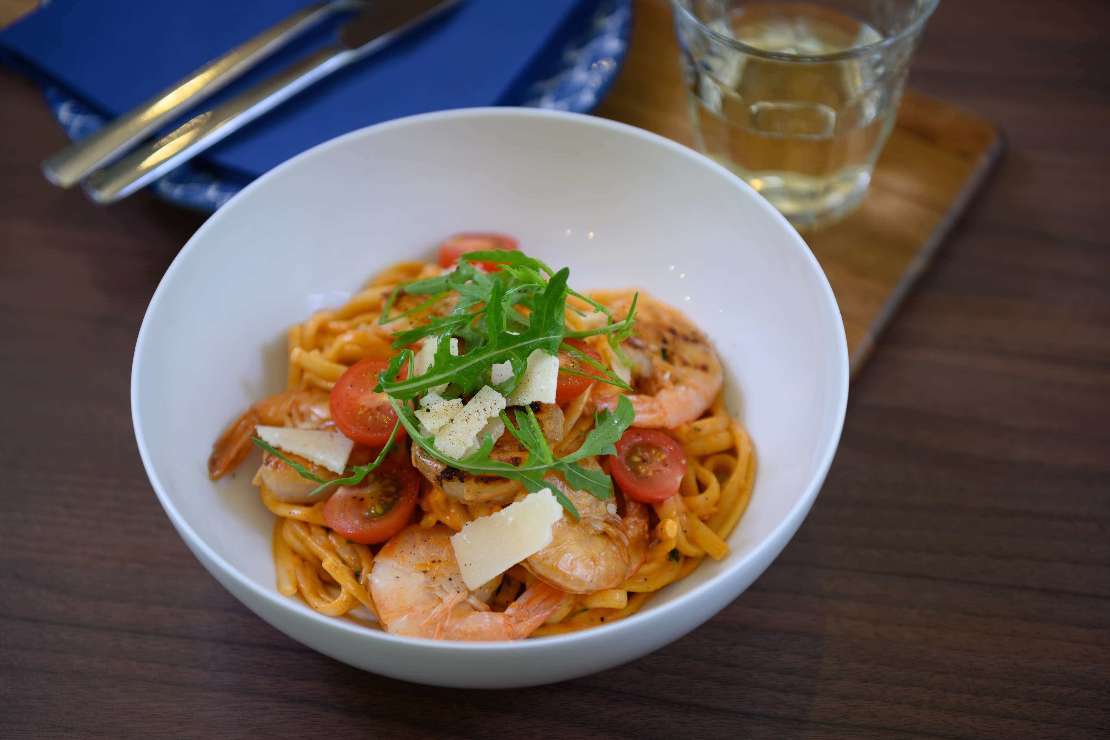 Un plato de pasta con camarones, tomates y queso sobre una mesa de madera.