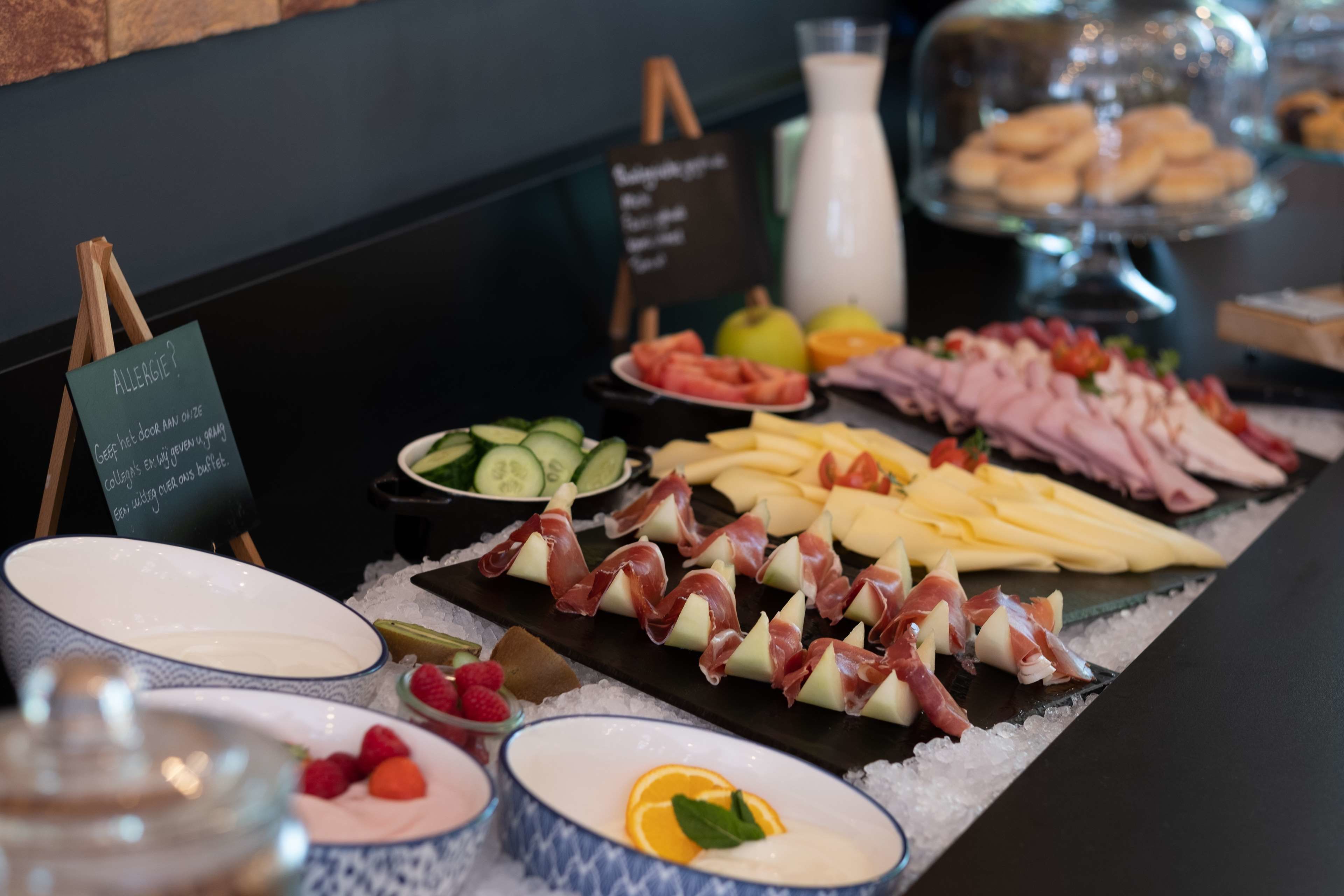 A buffet with various food items including cheese, meats, and fruits, with a sign indicating allergy information.