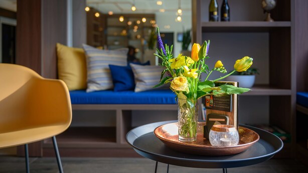 A modern living room with a round table, a yellow chair, and a blue sofa with striped cushions. - Tulip Inn Antwerpen (Antwerp)