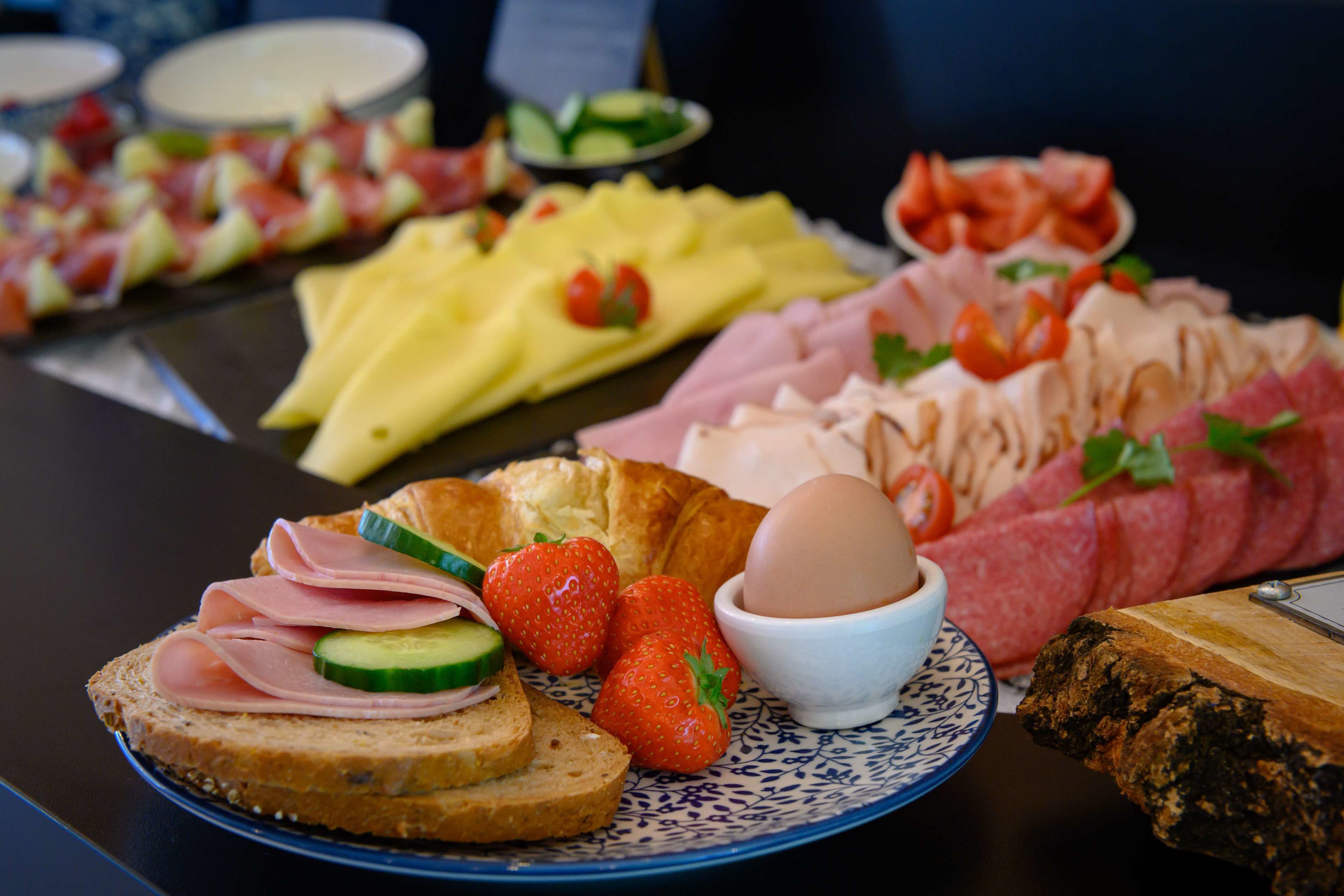 Un buffet de petit-déjeuner proposant divers aliments, notamment du pain, du jambon, des œufs, des fraises et un croissant.
