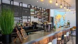 A modern bar with a wooden counter, bar stools, and a variety of liquor bottles. There is a chalkboard menu and a world map on the wall. - Tulip Inn Antwerpen (Antwerp)