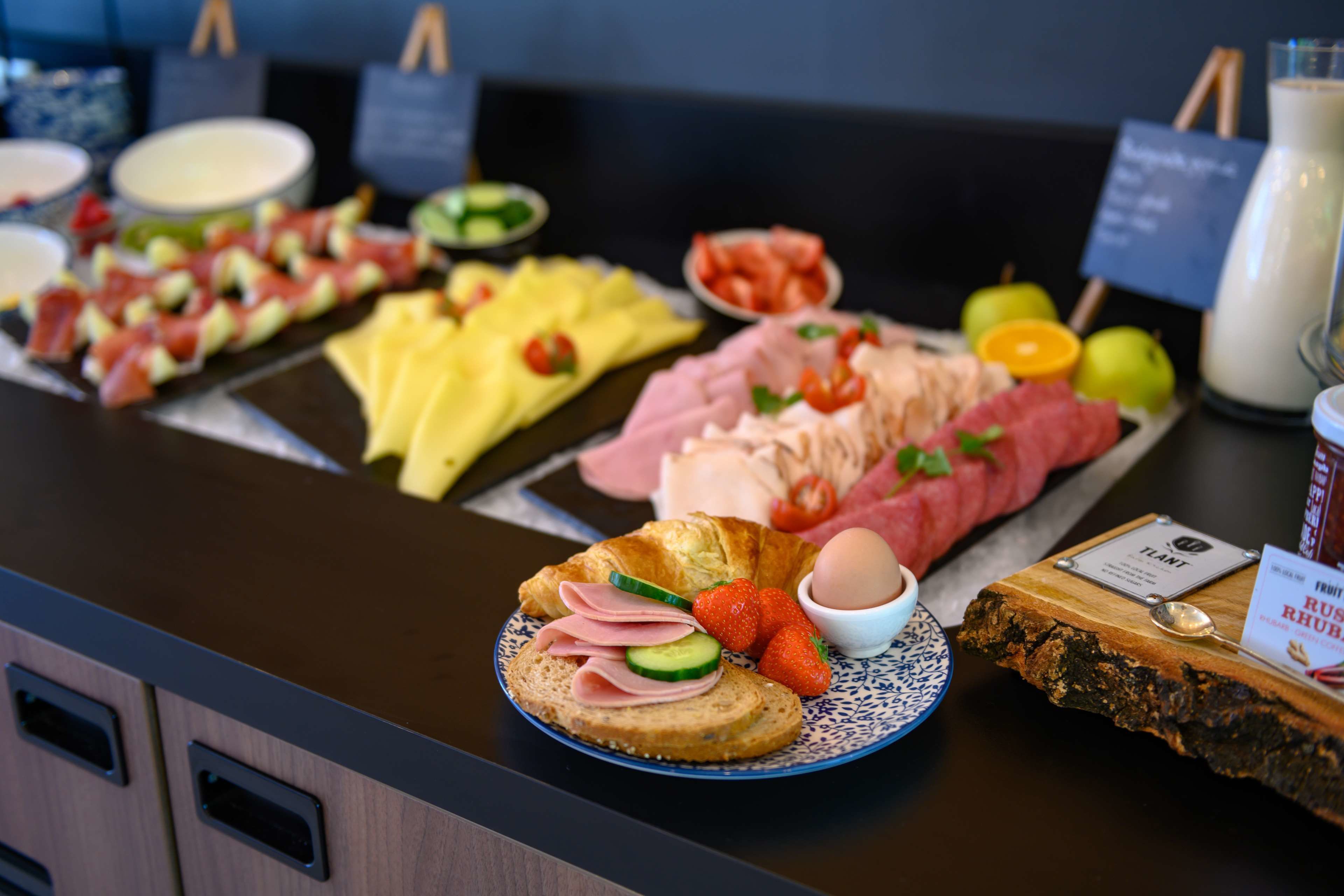 Un buffet con diverse pietanze tra cui carni, formaggi, frutta e un croissant.
