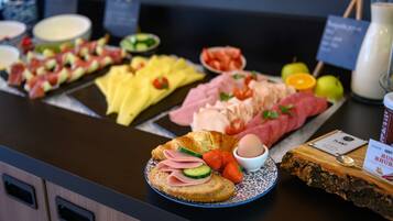 Un buffet con diverse pietanze tra cui carni, formaggi, frutta e un croissant.