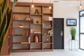A modern reception area with a wooden bookshelf, a potted plant, and a television on the wall.
