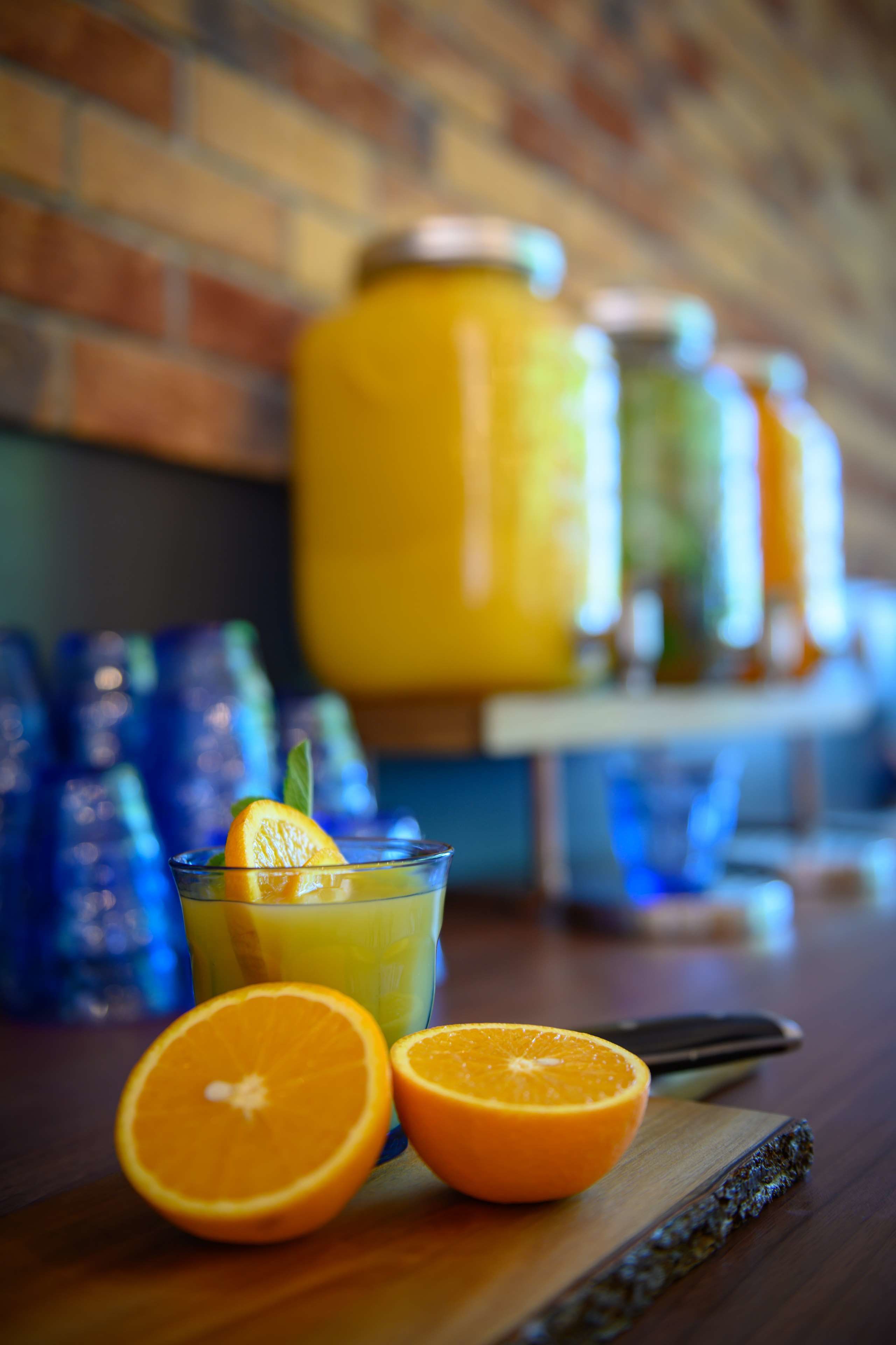 A glass of orange juice with a slice of orange on the rim, a half orange, and a knife on a wooden board.