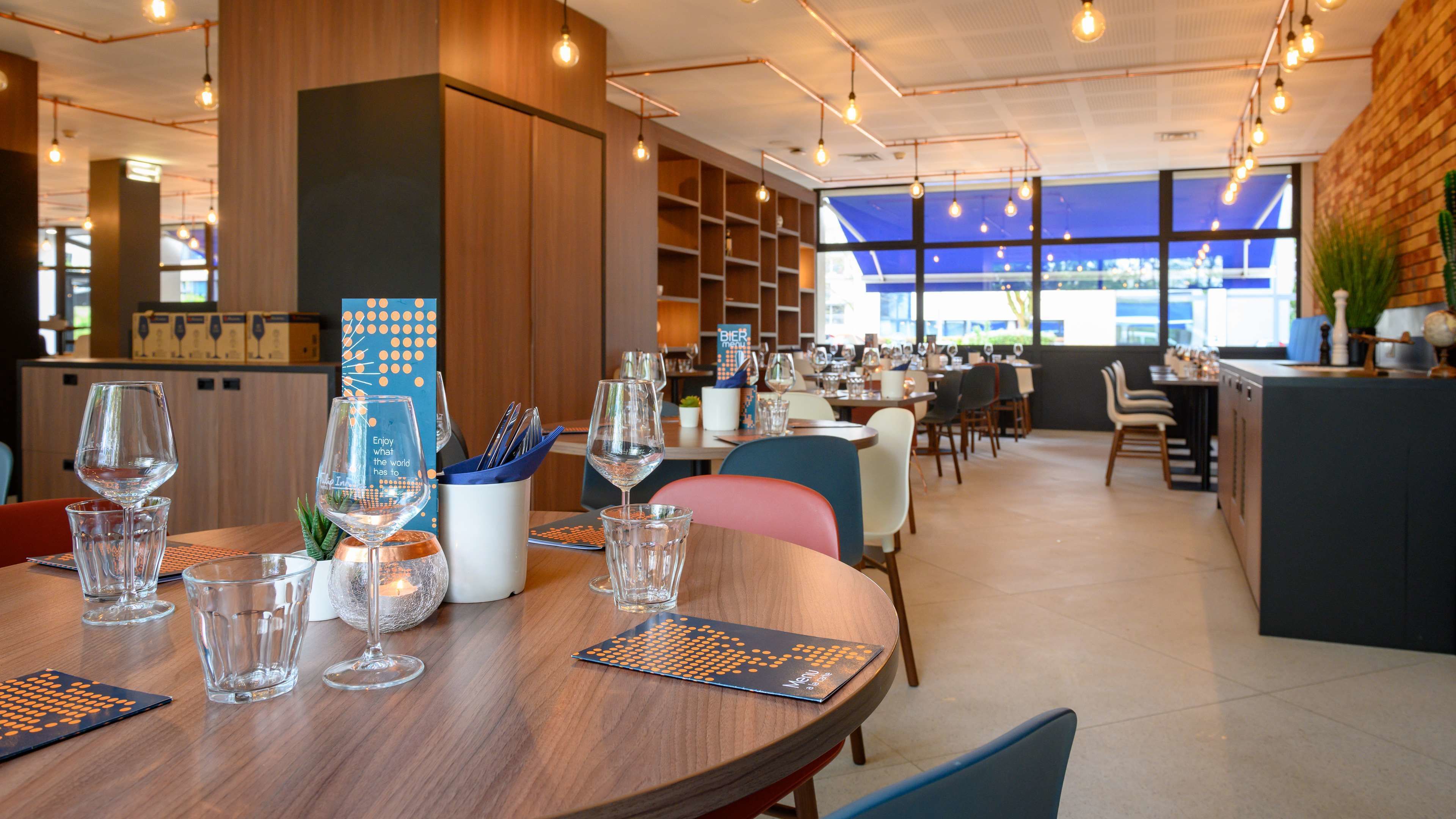 Un interior de restaurante moderno con mesas de madera, cristalería transparente y vistas a la ciudad a través de amplios ventanales.