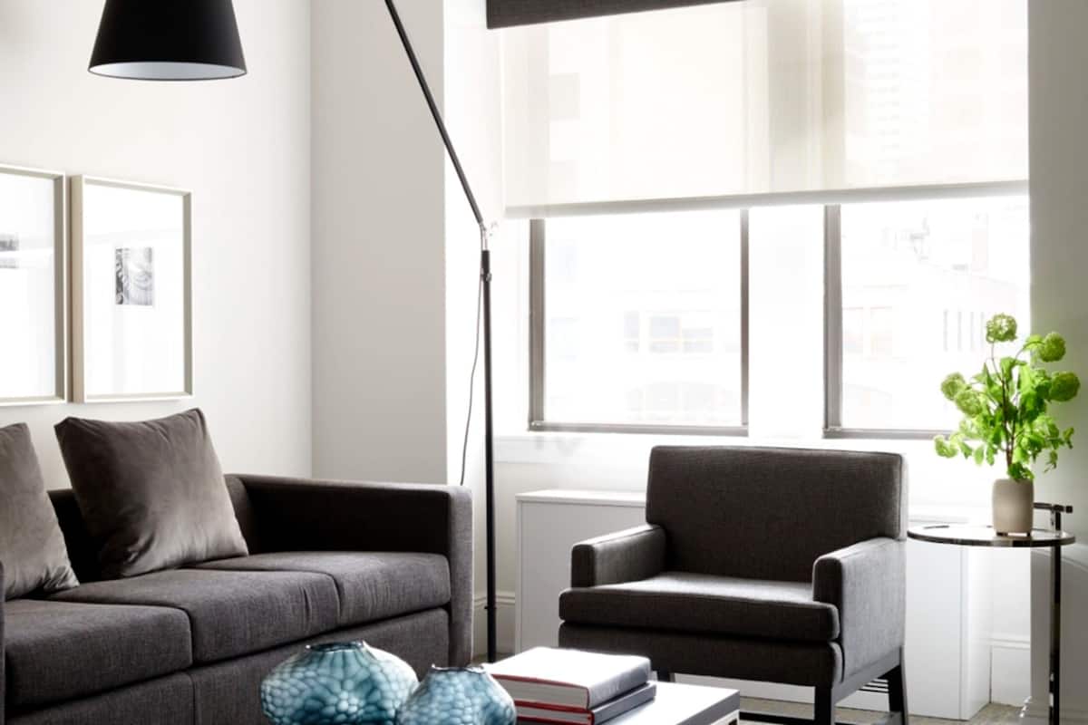 A modern living room with a grey sofa, a small round table, a floor lamp, and a potted plant.
