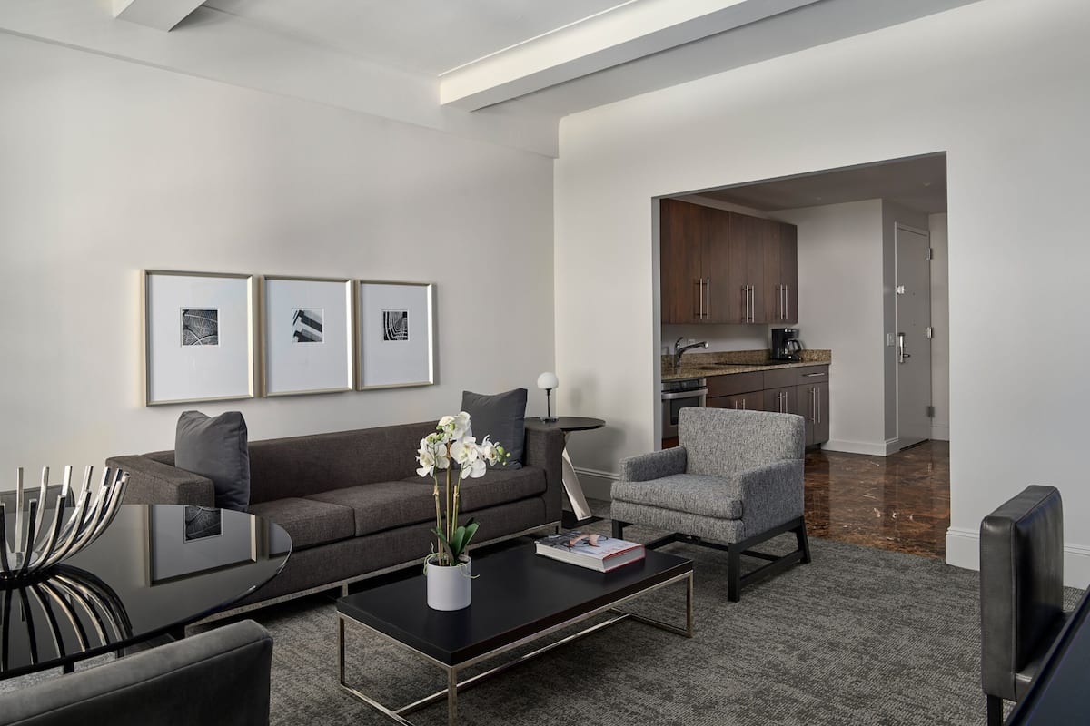 A modern living room with a sofa, armchair, coffee table, and artwork on the wall.