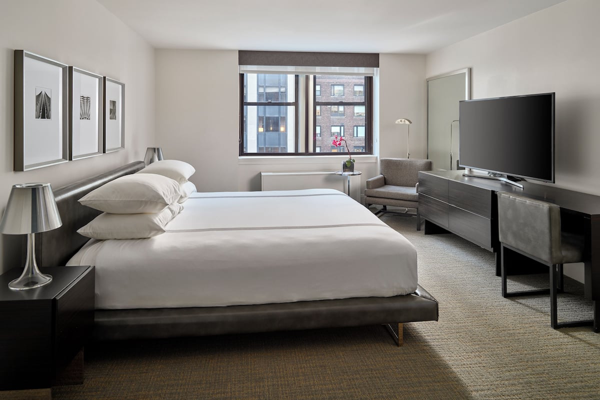 A modern hotel room with a large bed, a desk, a flat-screen TV, and framed pictures on the wall.