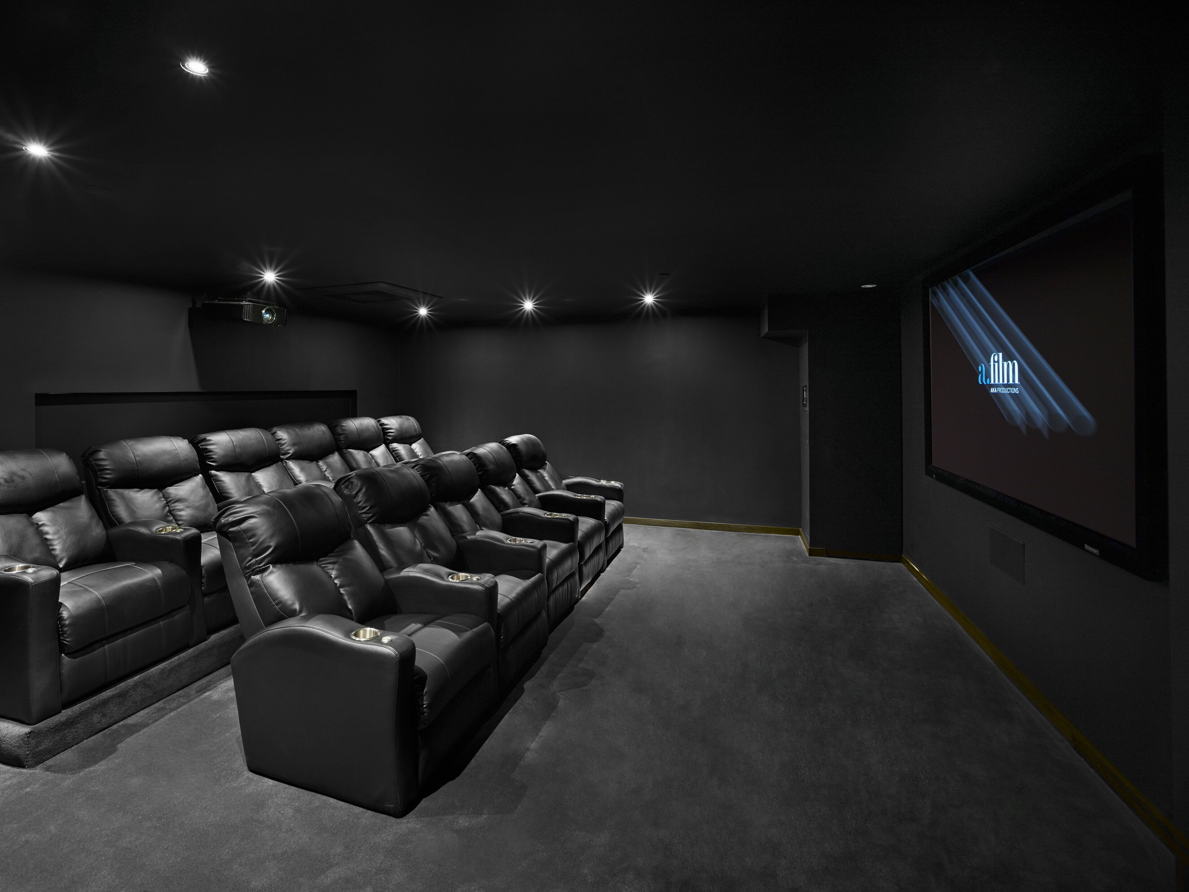 A dark-themed home theater with leather reclining seats and a large screen.
