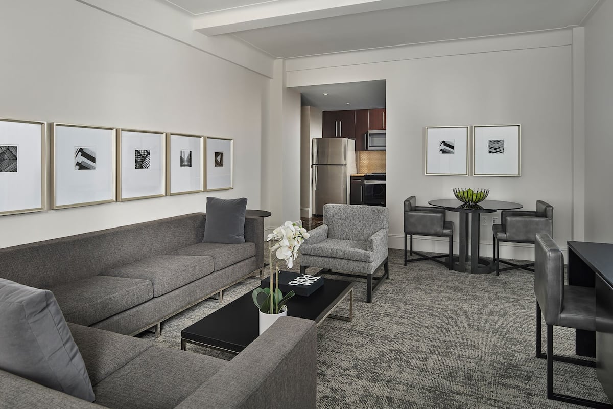 A modern living room with a grey sofa, a coffee table, and a dining area with a round table and chairs.