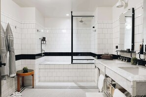 A modern bathroom with white tiles, a black accent wall, a glass-enclosed shower, a vanity with a mirror, and a small round table with a plant.