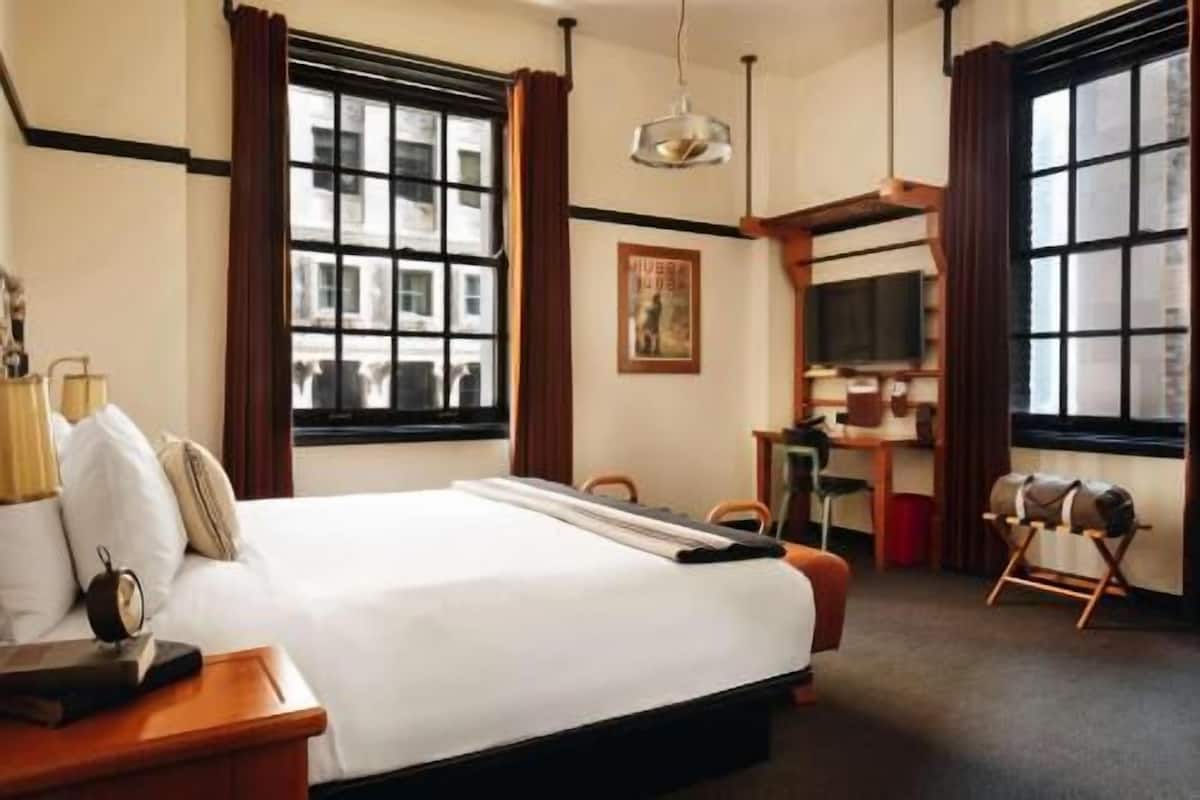 A hotel room with a large bed, a desk, a chair, a television, and a window with curtains.